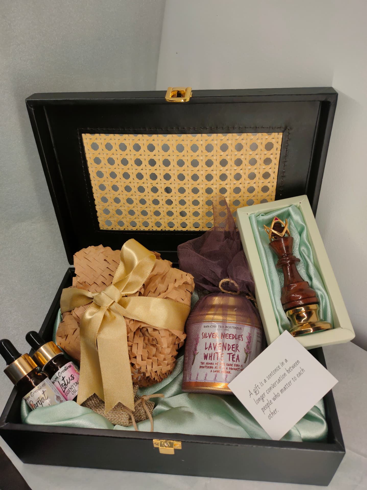 Open black case lined in mint satin holding oils, tea, a ribboned parcel, carved chess king and a handwritten card