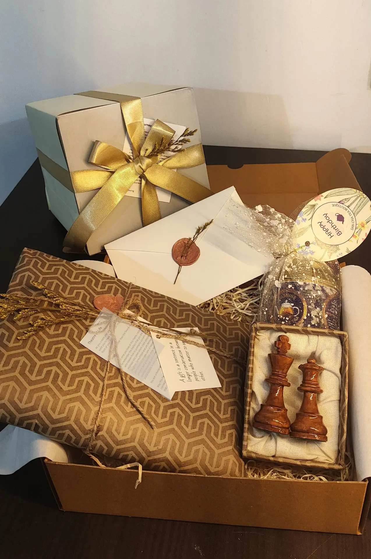 Open gift box with ribboned keepsake box, wax-sealed envelope, patterned wrap and carved chess pieces