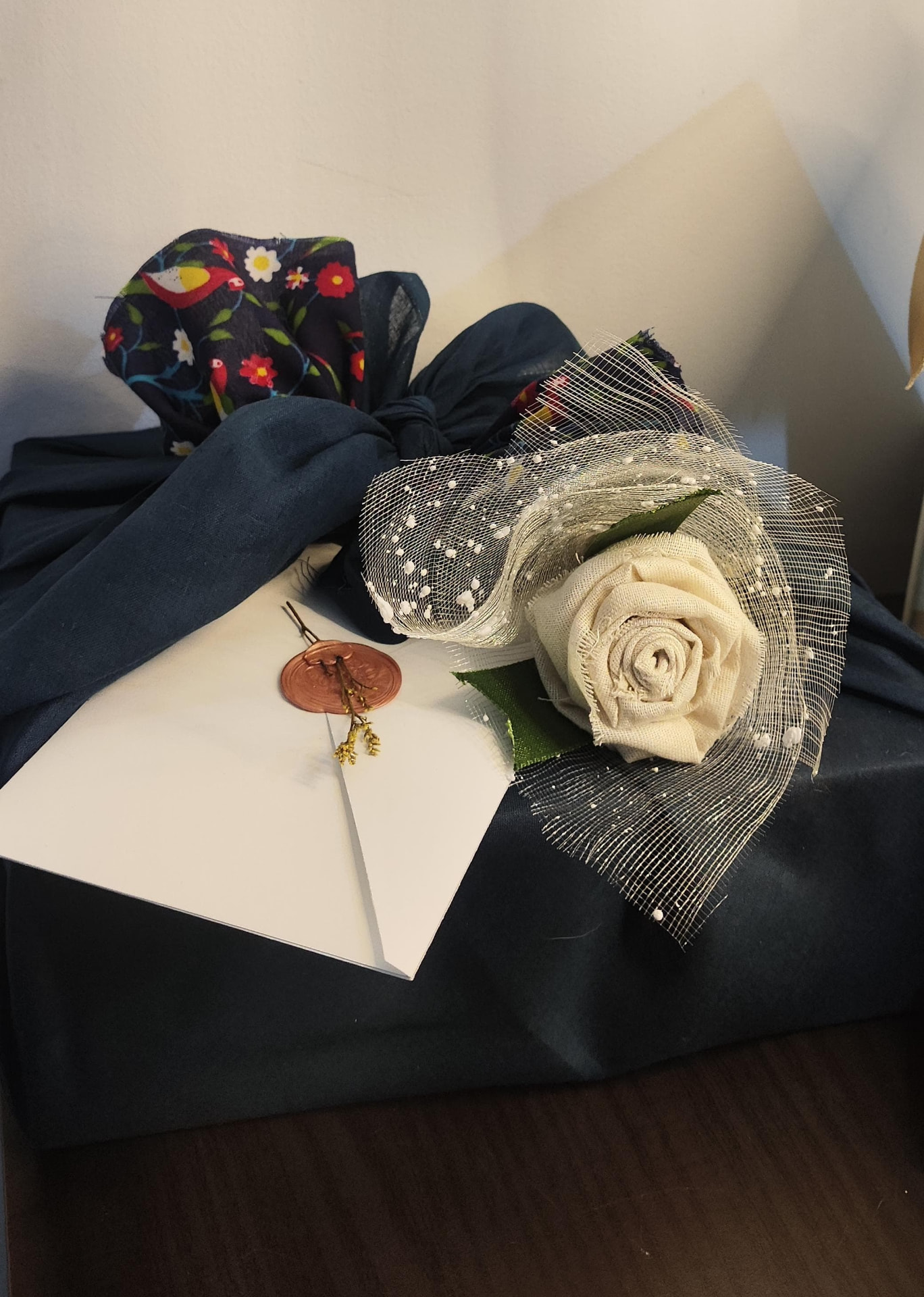 Navy fabric-wrapped gift with cloth rose and wax-sealed envelope