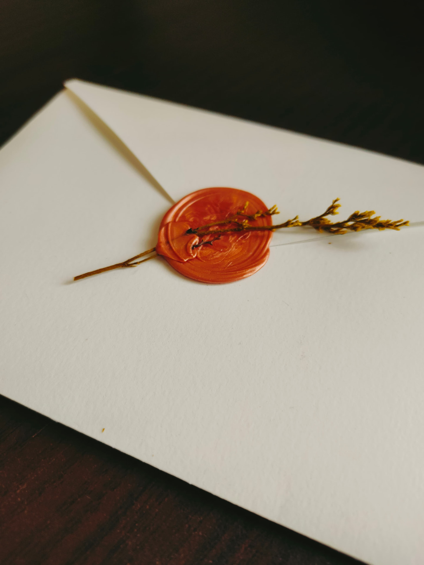 Cream envelope with orange wax seal and dried yellow sprig