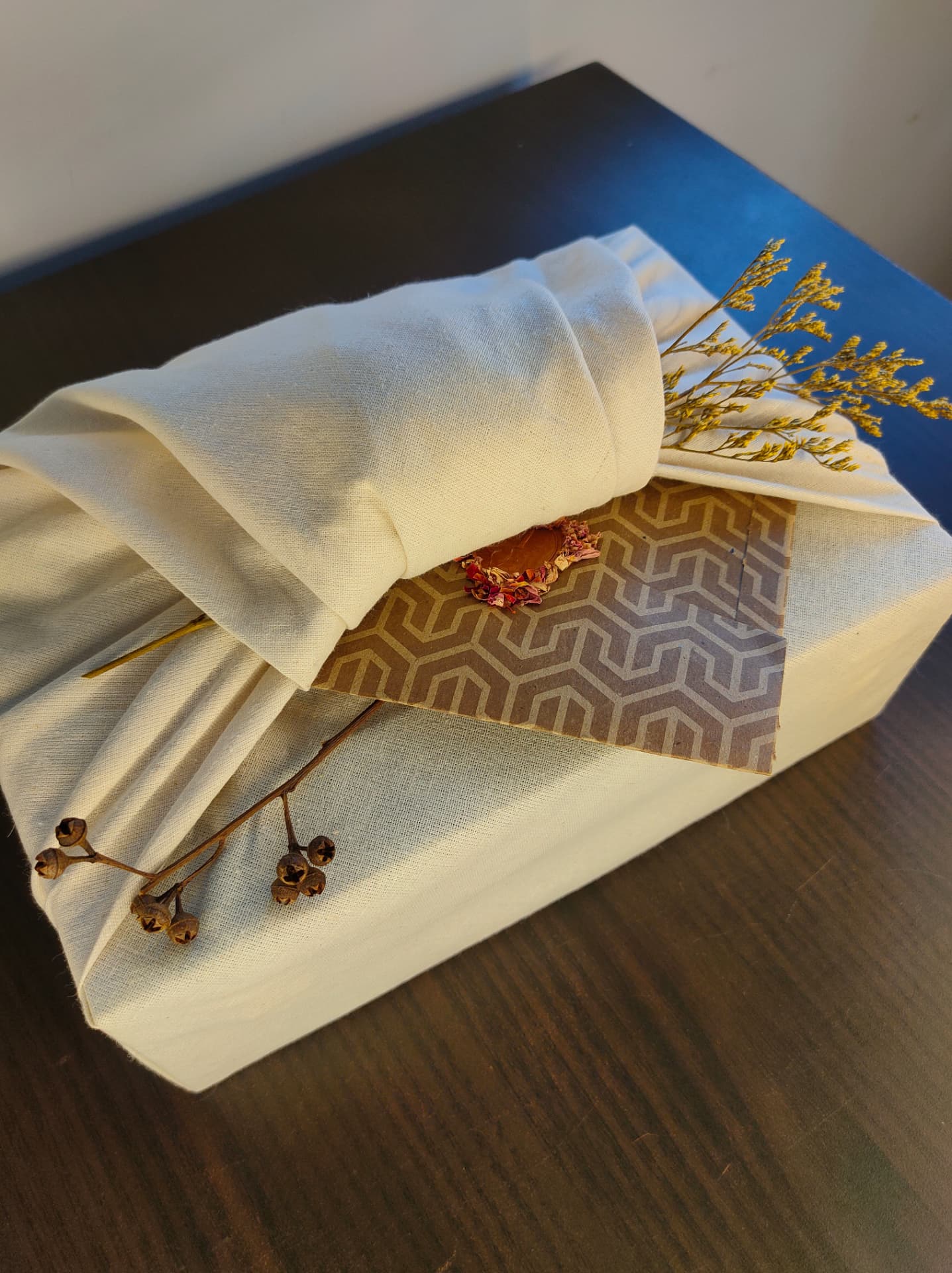 Cream cotton wrapped gift with wax seal, dried yellow sprigs and patterned kraft card