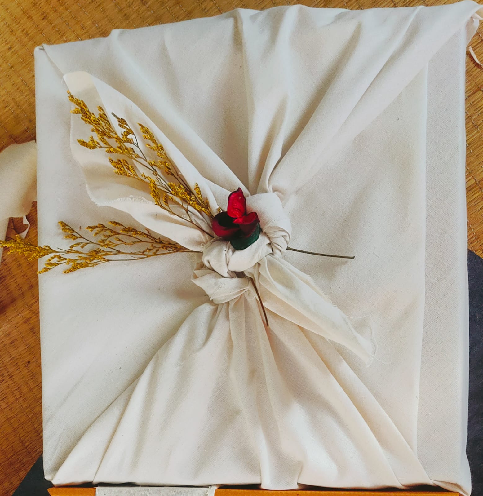 Cream cotton furoshiki wrap knotted with a red fabric rose and dried sprigs